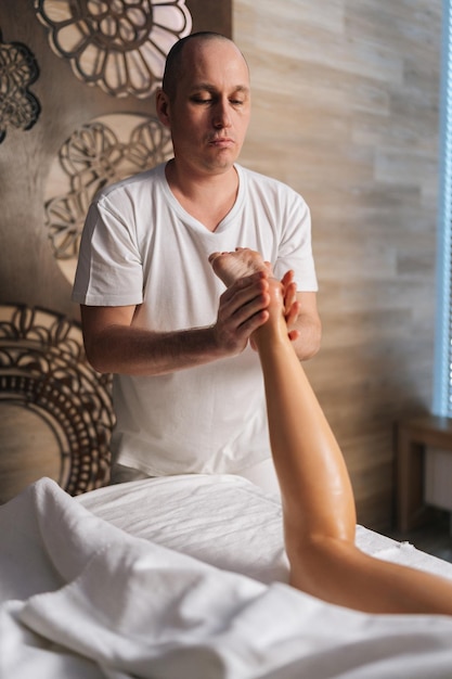 Verticaal portret van professionele mannelijke masseur die de hiel van de voet masseert van een onherkenbare vrouwelijke cliënt die op een massagetafel ligt in de spa salon