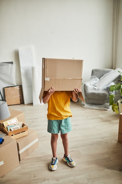 Verticaal portret van volledige lengte van tiener met doos op hoofd die met dingen speelt terwijl familie beweegt...