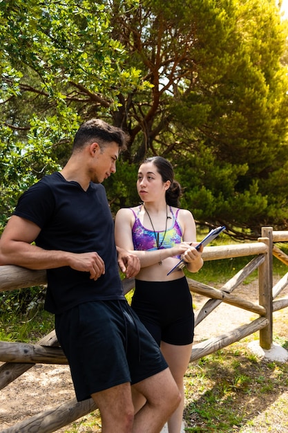 verticaal portret van vrouwelijke personal trainer die oefenschema voor training uitlegt aan jonge man buitenshuis