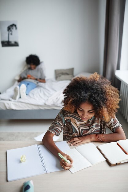 Verticaal portret van vrouwelijke student die huiswerk doet en in de ruimte van het notitieboekje schrijft