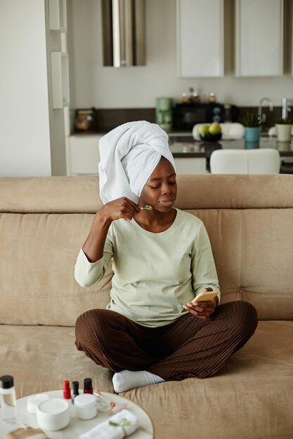 Verticaal portret van zwarte jonge vrouw met haar gewikkeld in een handdoek die thuis geniet van een zelfzorgdag