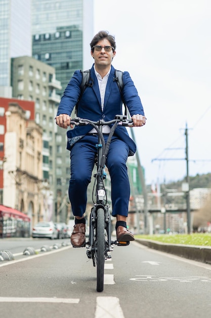 Foto verticaal portret zakenman op een elektrische fiets op een stadsfietspad met zonnebril en rugzak