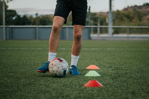 Foto verticaal schot van de benen van de speler die kegels op grasveld dribbelen.