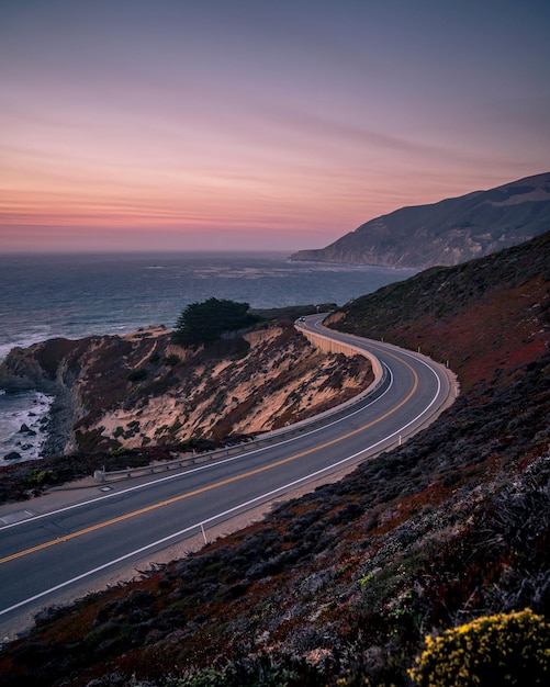 Verticaal schot van de snelweg aan de Pacifische kust omringd door gras in Californië tijdens zonsondergang