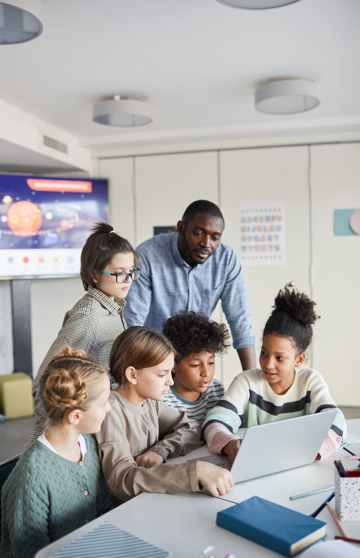 Foto verticaal schot van diverse groep kinderen die samen laptop gebruiken aan tafel in moderne school