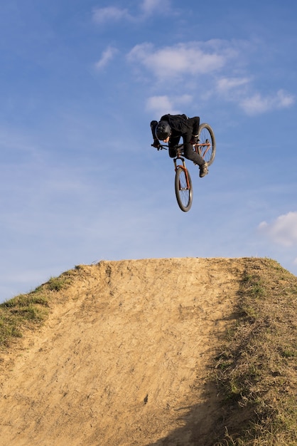 Verticaal schot van een fietser die over een helling springt op een blauwe hemelachtergrond