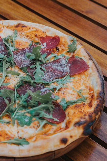 Verticaal schot van een heerlijke pizza met vlees en rucola op een dienblad op tafel