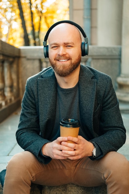 Verticaal schot van een kale man die geniet van koffie en muziek terwijl hij op de trap zit