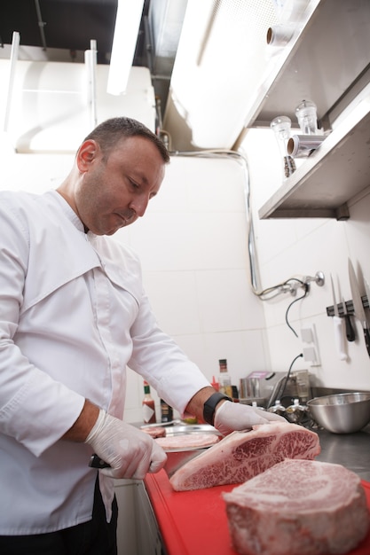 Foto verticaal schot van een mannelijke chef-kok die in zijn keuken werkt en rundvlees snijdt