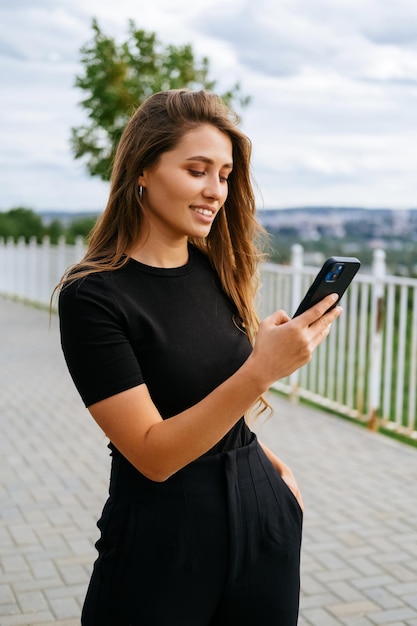 Verticaal schot van een moderne vrouw die buiten staat terwijl ze naar de telefoon kijkt