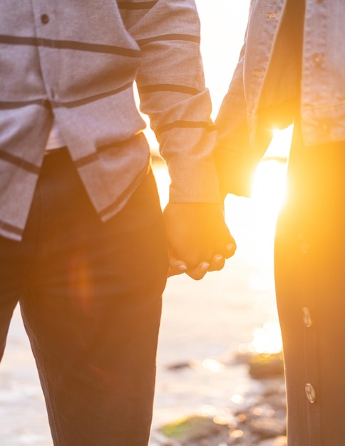 Verticaal schot van een paar hand in hand met een prachtige zonsondergang op de achtergrond