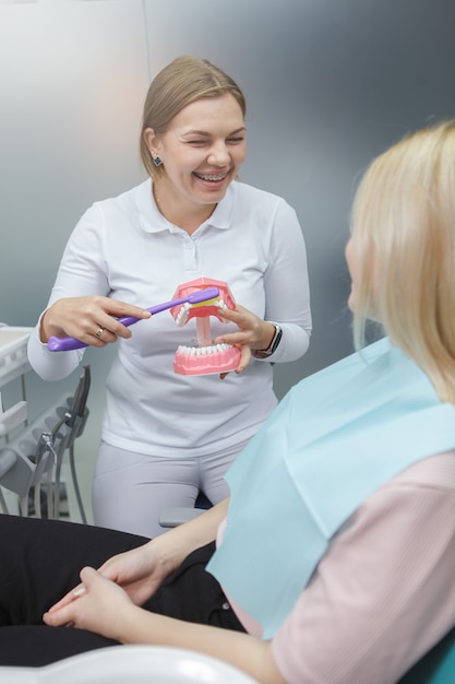 Verticaal schot van een vrouwelijke dentis die haar patiënt toont hoe tanden correct op kaakmodel te poetsen