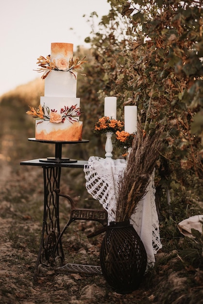 Verticaal schot van een witte bruidstaart met oranje versieringen en kaarsen in de tuin