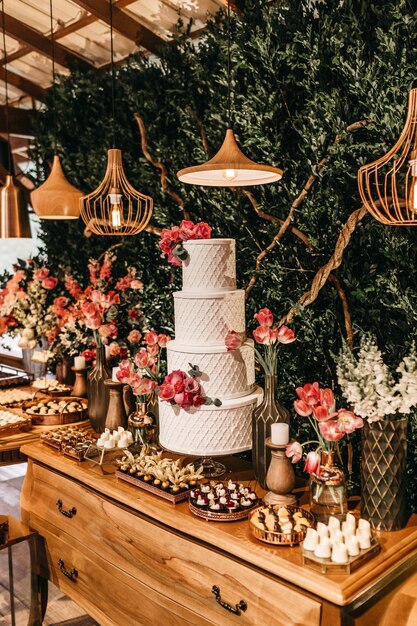 Verticaal schot van een witte cake met rode bloemen en zoete snacks op een houten tafel in een evenementenlocatie