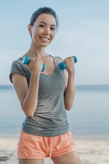 Verticaal schot van fitte jonge vrouw met halters op het strand die aan het trainen zijn