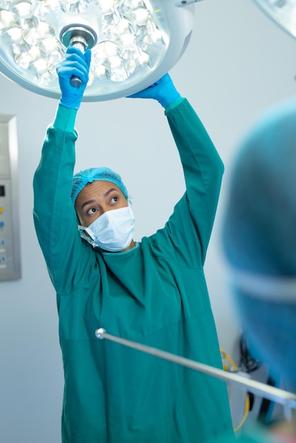 Foto verticaal van biraciale vrouwelijke chirurg die de lichten in de operatiekamer aanpast voor operatie, kopieerruimte. ziekenhuis-, medische en gezondheidszorgdiensten.