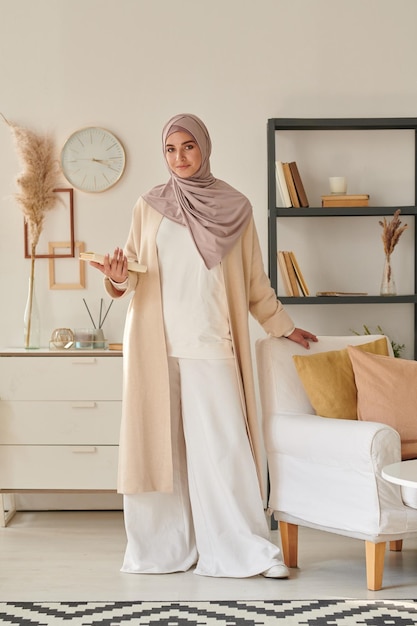 Verticaal volledig geschoten portret van een aantrekkelijke moslimvrouw die een stijlvolle, casual outfit draagt met een hijab-greep