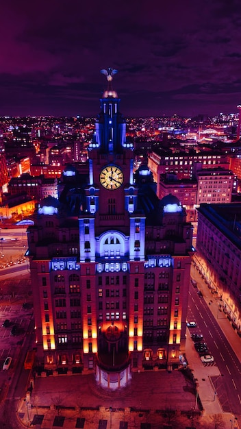 Foto vista aerea verticale di un edificio storico illuminato di notte con le luci della città sullo sfondo a liverpool, regno unito