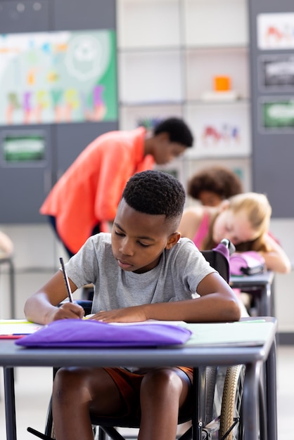 Vertical of african american schoolboy in wheelchair sitting at desk working in class copy space