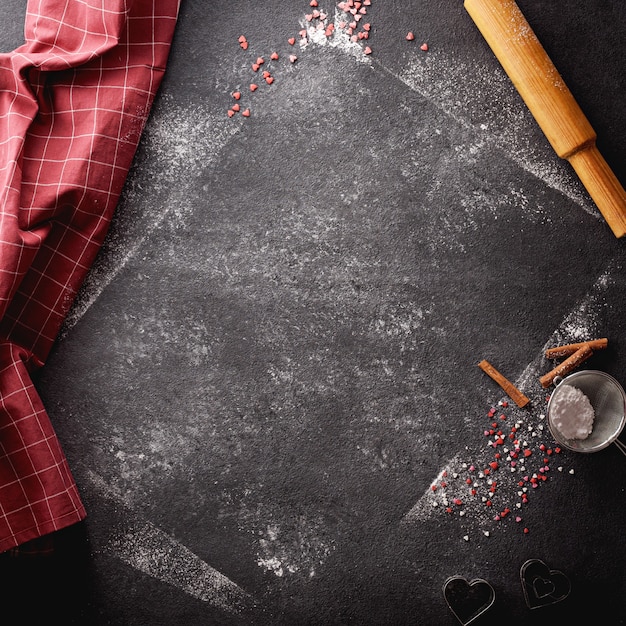 Foto sfondo nero verticale cosparso di farina e zucchero a velo e con utensili da cucina
