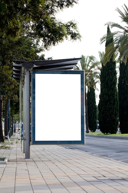 Vertical blank billboard on the city street with green trees