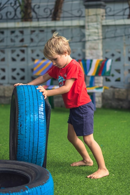 VERTICAL Boy play practice balance motor coordination training Jump go step carry car tires Concept outdoor fun open air sport game classes obstacle course for child improve efficiency raising son