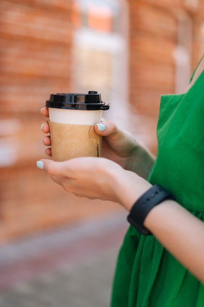 街の通りで屋外でテイクアウトのコーヒーカップを保持している若い女性の垂直クローズアップクロップドショット