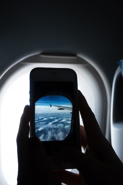 Photo vertical close-up of hands photographing an airplane window with a cell phone, with copy space.
