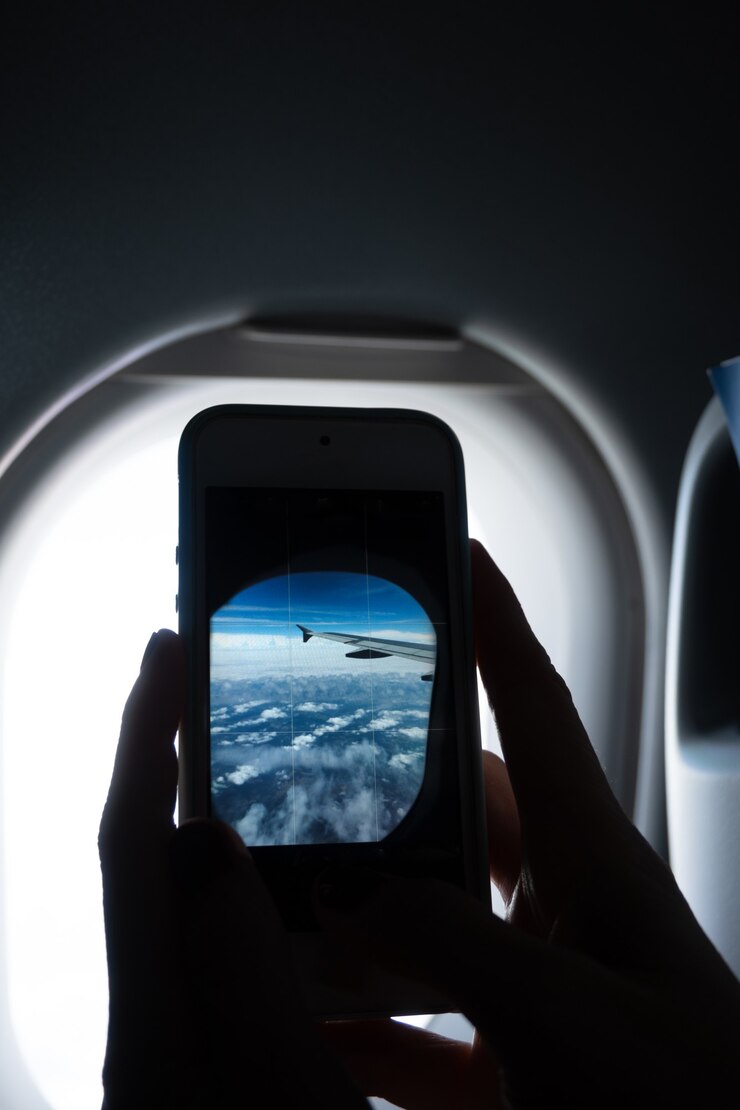 Vertical close-up of hands photographing an airplane window with a cell phone, with copy space.
