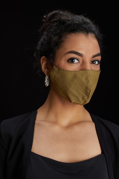 세로 파티에서 검은 배경에 포즈를 취하는 동안 얼굴 마스크를 쓰고 우아한 중동 여자의 초상화를 닫습니다