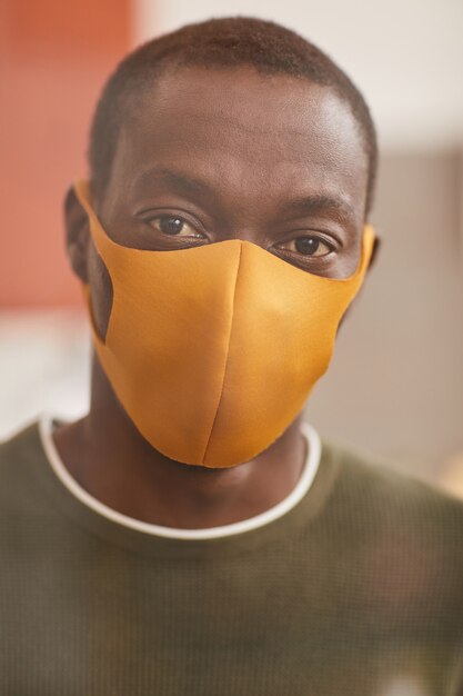 Vertical close up portrait of modern African-American man wearing yellow mask and looking at camera