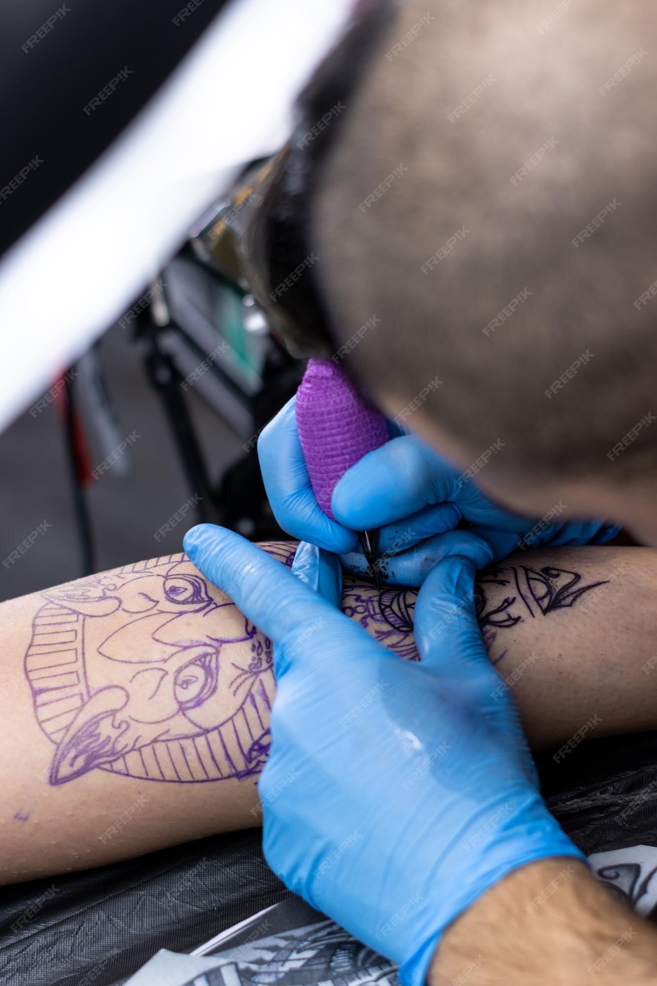 Premium Photo | Vertical closeup of an alternative tattooist tattooing a client39s skin with blue protective gloves in his small tattoo studio Premium Photo | Vertical closeup of an alternative tattooist tattooing a client39s skin with blue protective gloves in his small tattoo studio