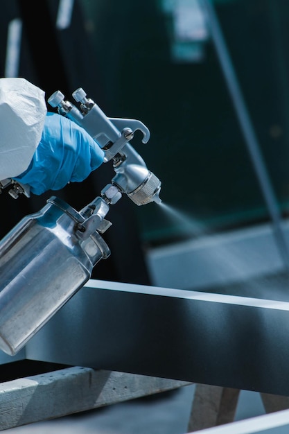 Vertical closeup of a person wearing a protective suit and gloves spraypainting in a workshop