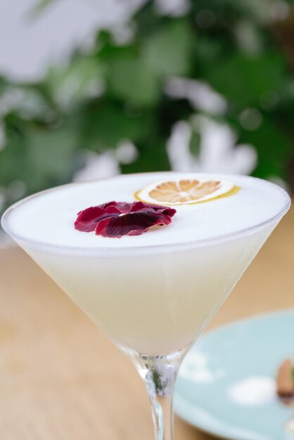 Vertical closeup shot of a white cocktail with a lemon slice and a red flower in a martini glass