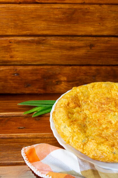 Vertical closeup of spanish omelette with checkered napkin orange tones on dark wooden background