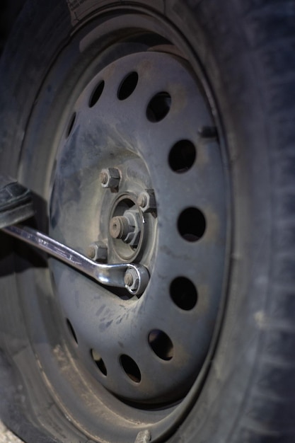 Photo vertical detail of an unrecognizable mechanic loosening lug nuts to change a flat tire on a vehicle