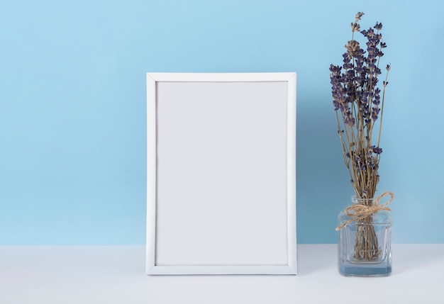 Vertical emply spring white photo frame mockup on a blue background with lavender flowers in a vase. Women's day concept.