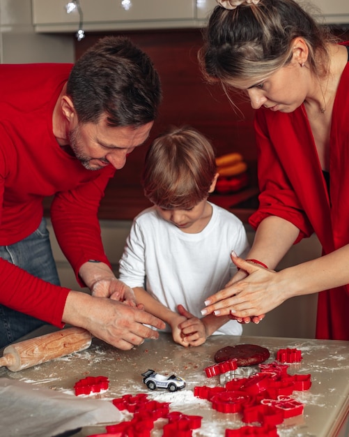 Vertical family photo Dad mom child son boy 4 years bake cookies Teamwork Happy family Christmas baking at home in kitchen dressed in red color