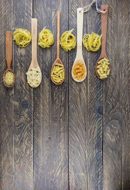 Vertical flat view of wooden spoons with different kinds and shapes of dry pasta. wooden rustic planks.