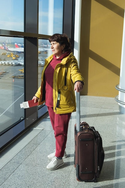 Photo vertical full length portrait of an elderly woman with a suitcase passport and boarding pass