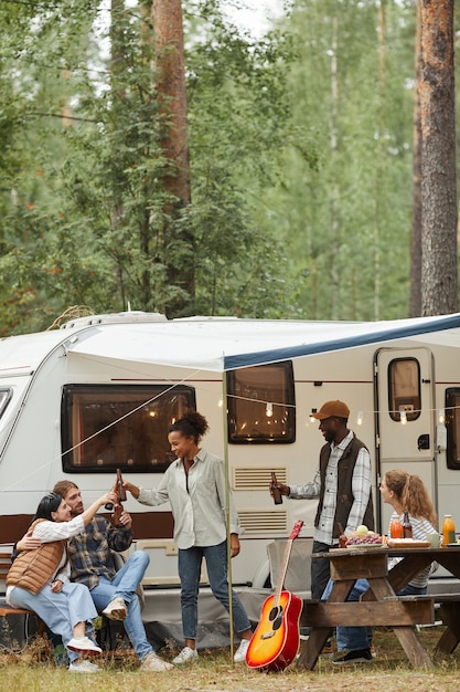 Vertical full length portrait of friends enjoying outdoors while camping with van in forest copy space