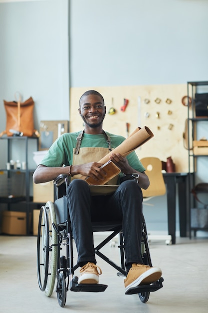 Vertical full length portrait of smiling africanamerican man using wheelchair enjoying work in leath...