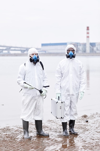 Vertical full length portrait of two people wearing protective\
suits and looking at camera outdoors ...