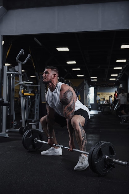 Vertical full length shot of a strong muscular tattooed male athlete working out at fumctional training gym lifting barbell