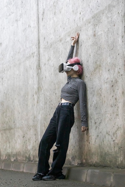 Vertical fulllength photo of young lady wears VR set and leaning on wall