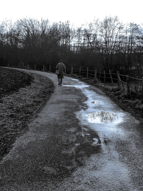 Photo vertical grayscale shot of a man walking through a path with puddles