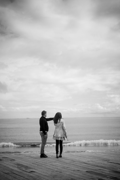 Vertical grayscale shot of two people enjoying the view on a pier