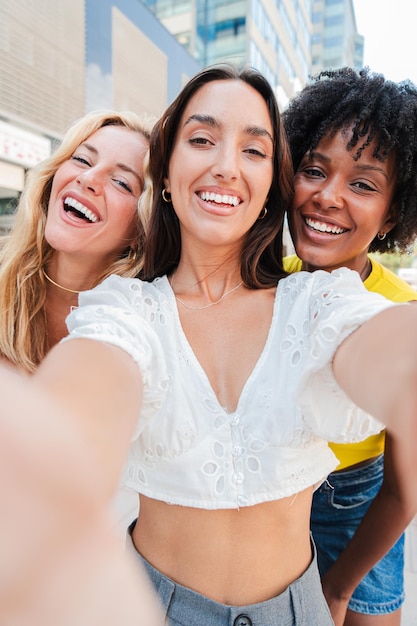 vertical group of three happy young women taking a selfie together outdoors capturing a fun moment