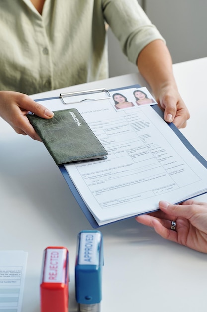 Vertical high angle of unrecognizable woman applying for work visa giving set of documents to consul