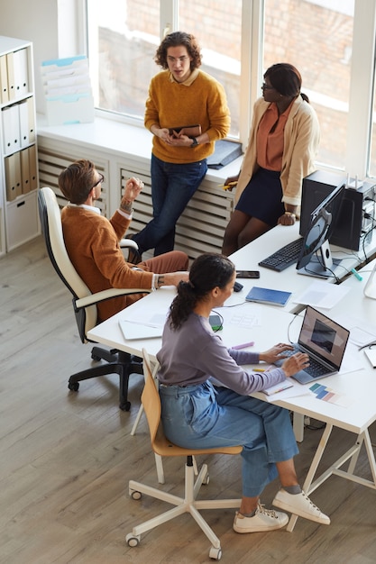 Vertical high angle view at multi-ethnic IT development team collaborating on business project while working in software production studio